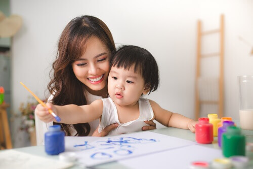 Smiling woman helping a toddler paint.