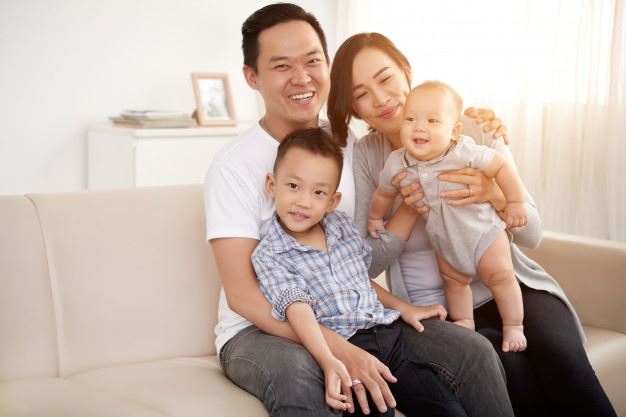 Smiling man with a young boy on his lap sitting next to a smiling woman holding a baby.